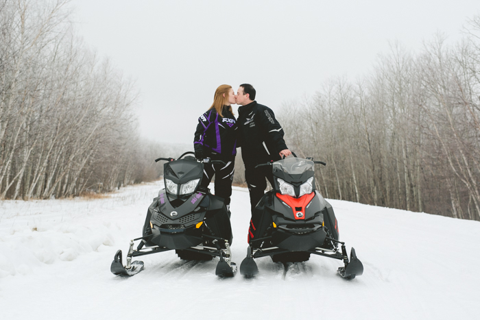 engagement photo of couple kissing on skidoo snowmobiles