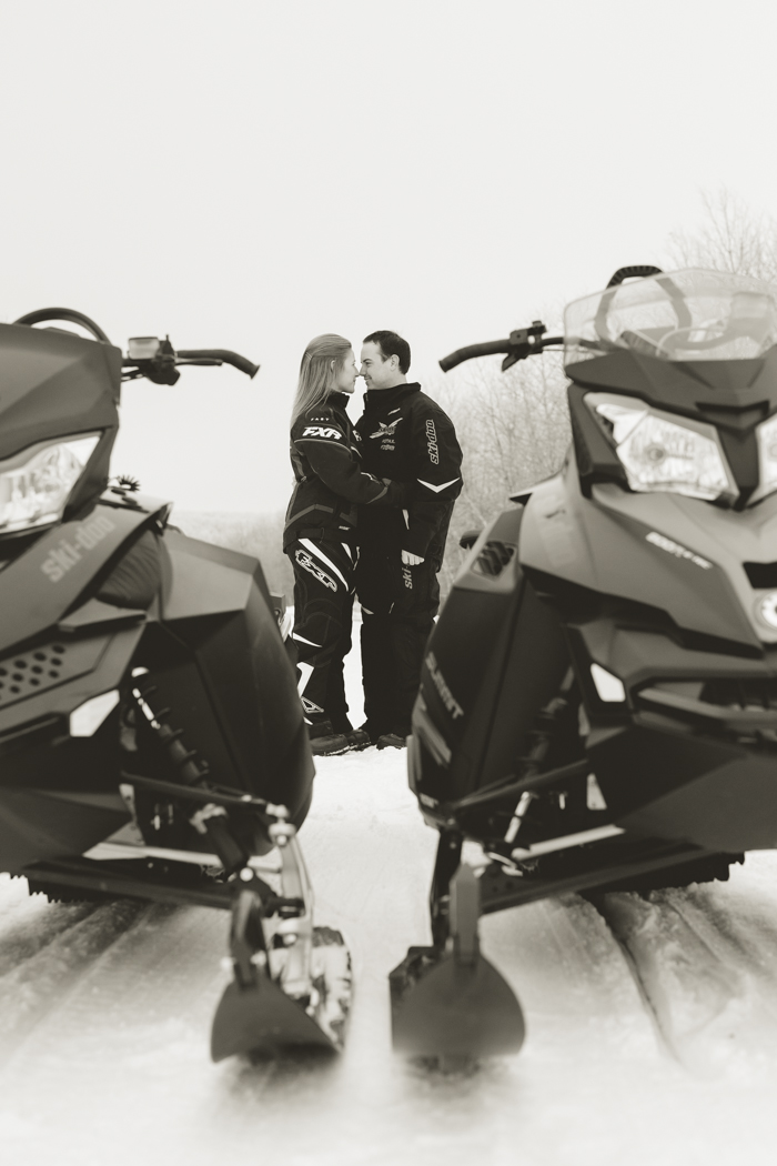adventurous couple kissing near their skidoo snowmobiles