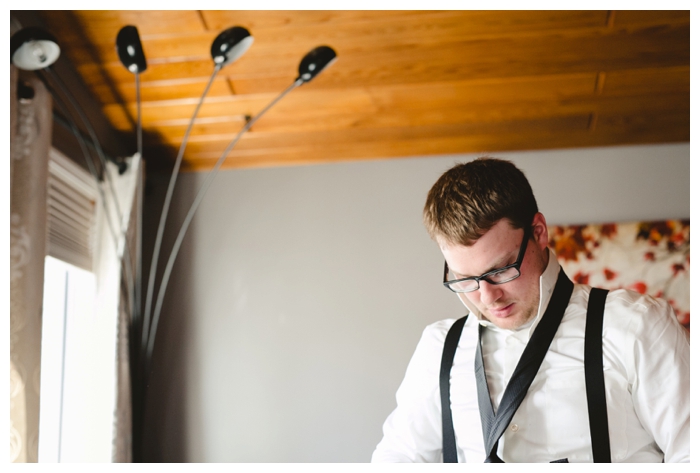 photo of groom getting dressed in black tie and white shirt with suspenders