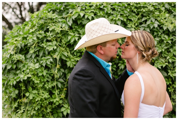 romantic photo of bride and groom standing in front of green vines while kissing