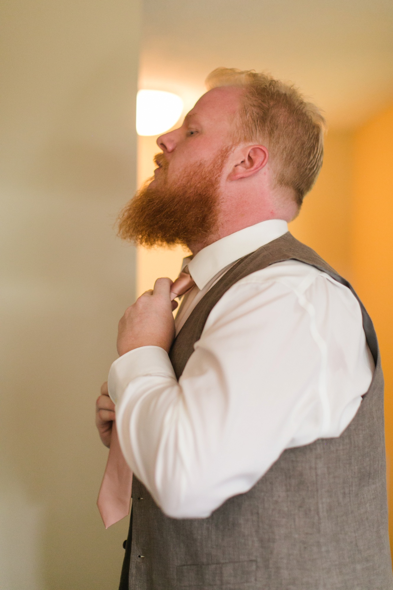 Bearded groom putting on wedding suit